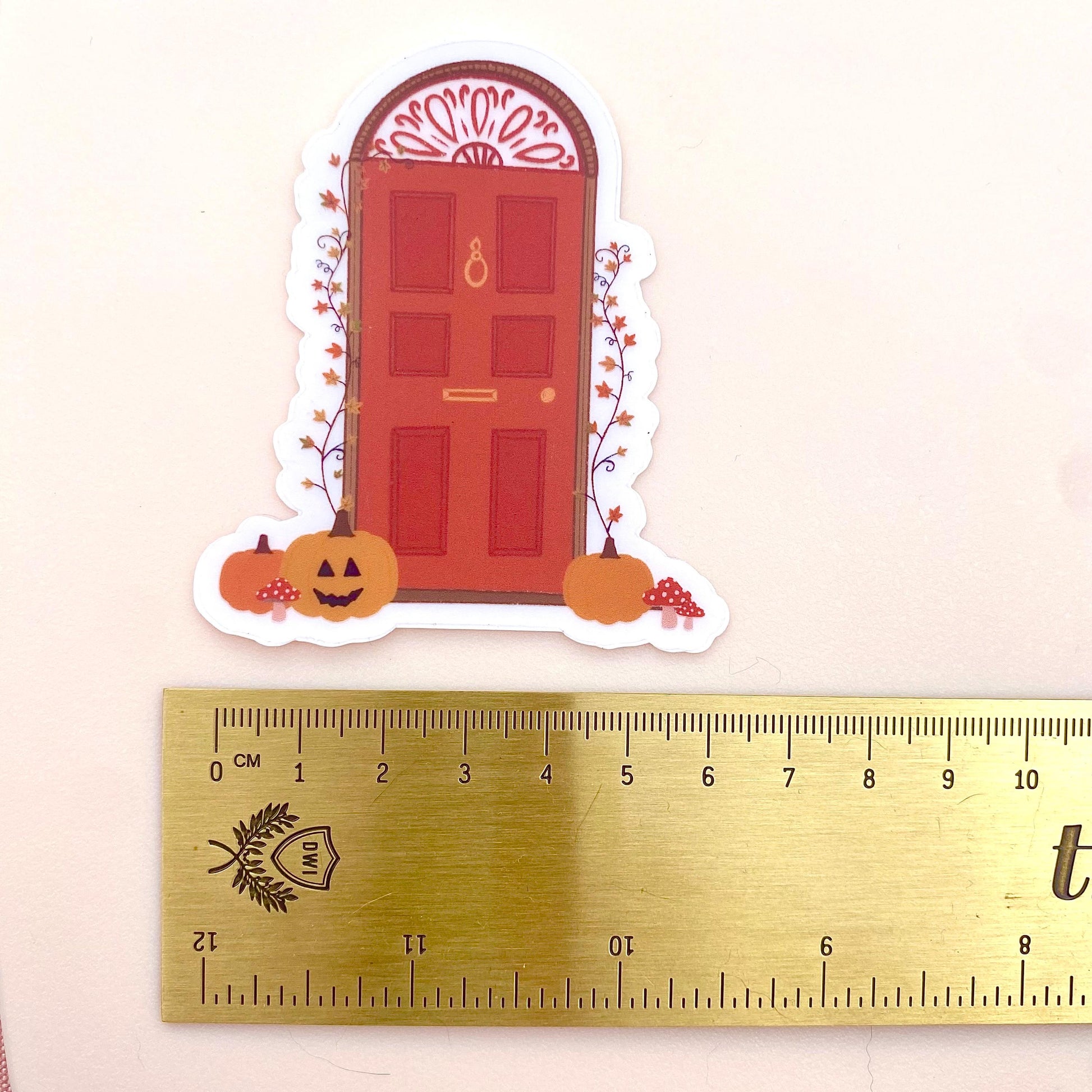 Decorative Halloween door sticker with pumpkins and a red door on a white background with a gold ruler for scale..