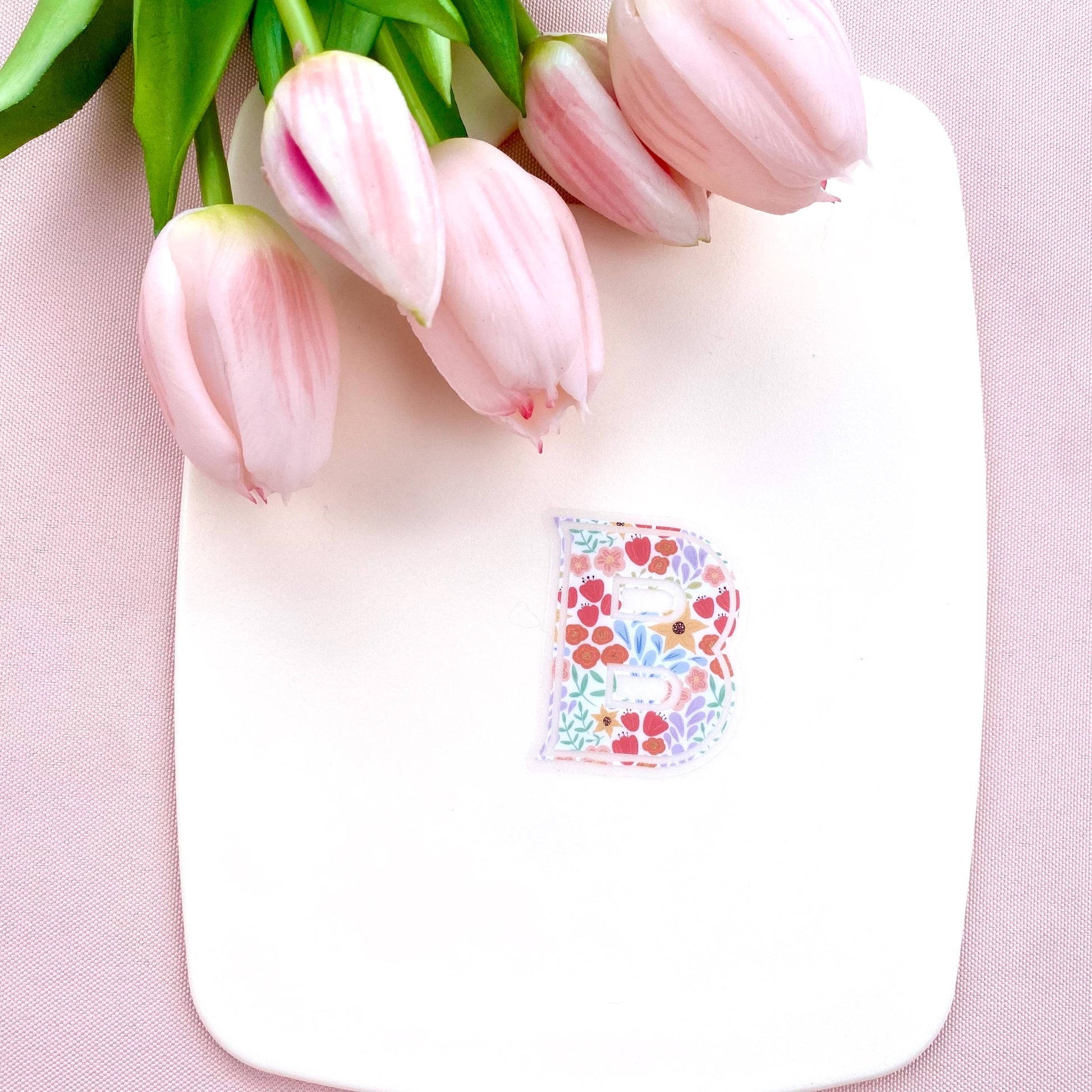 Pink tulips on a white board with a floral letter 'B' sticker on a pink background