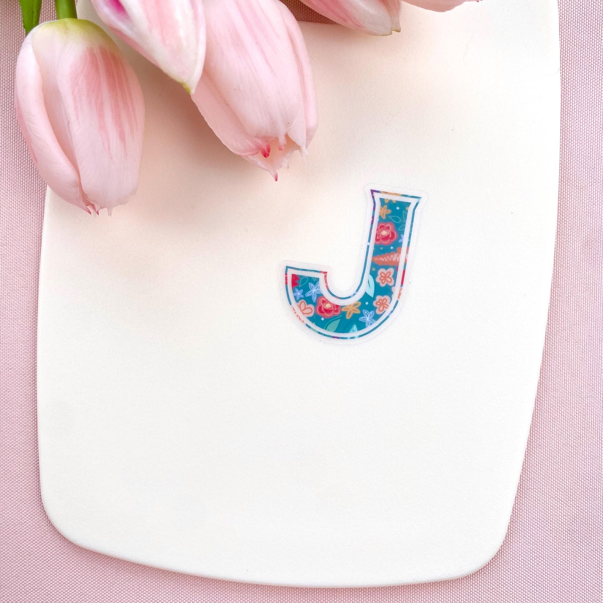 Colourful letter 'J' sticker on a pink background with tulips.