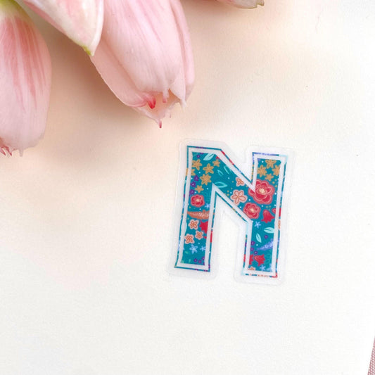 Colourful floral letter 'N' sticker on a light background with pink flowers.