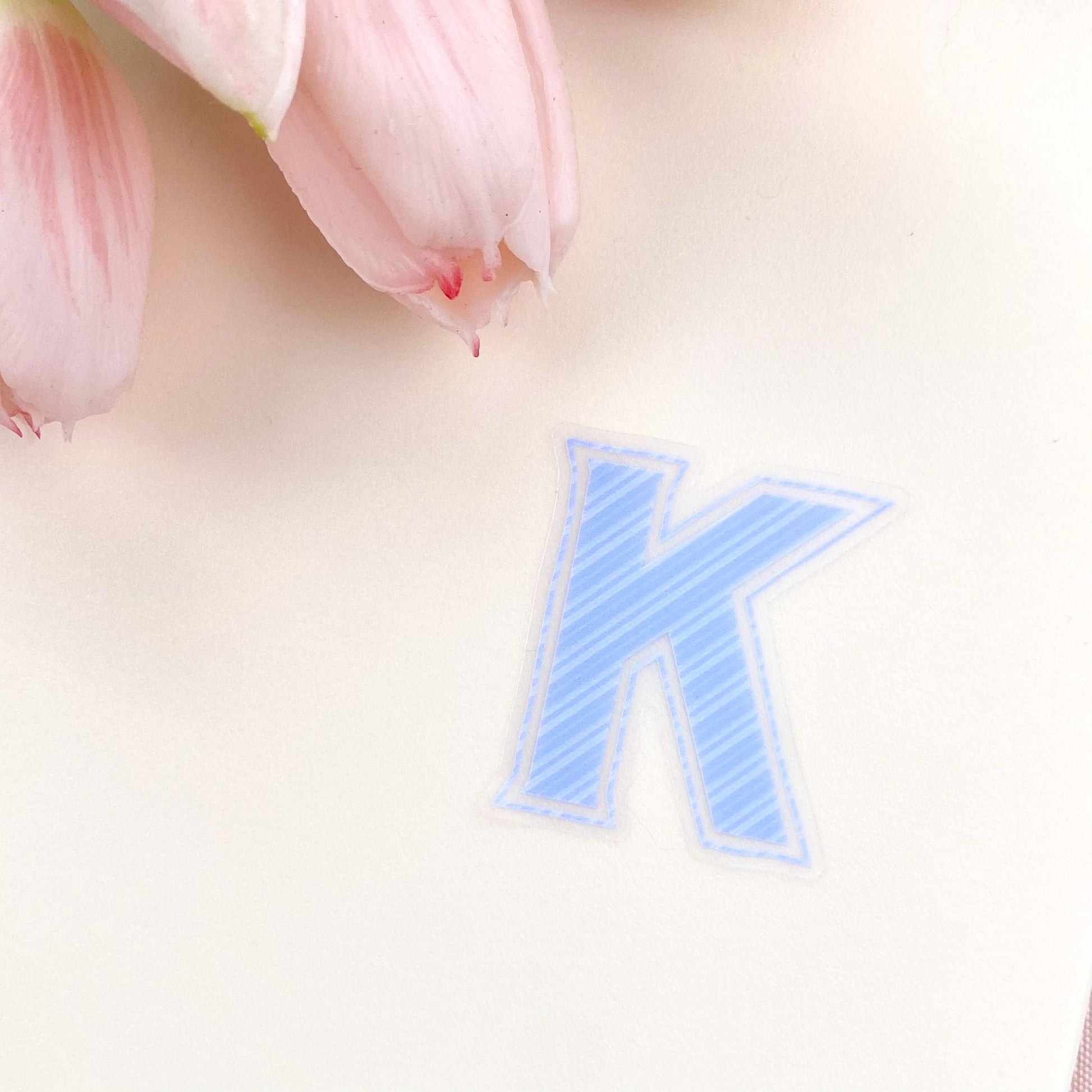 Blue striped letter 'K' transparent sticker against a white background