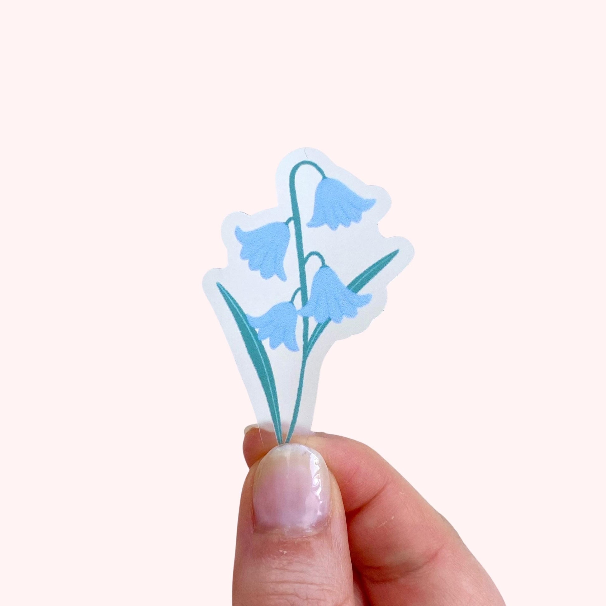 Hand holding a bluebell flower sticker against a white background