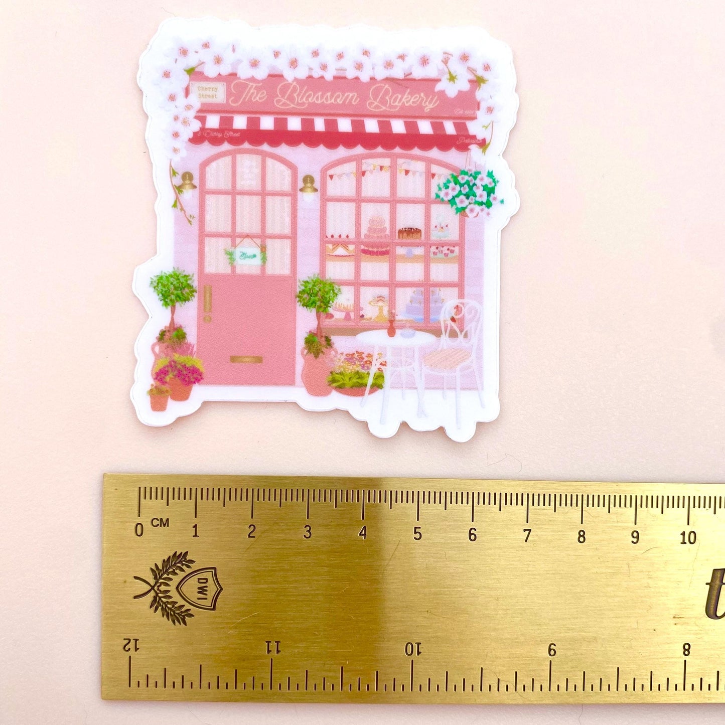 Sticker of a pink bakery with a ruler for scale on a light pink background