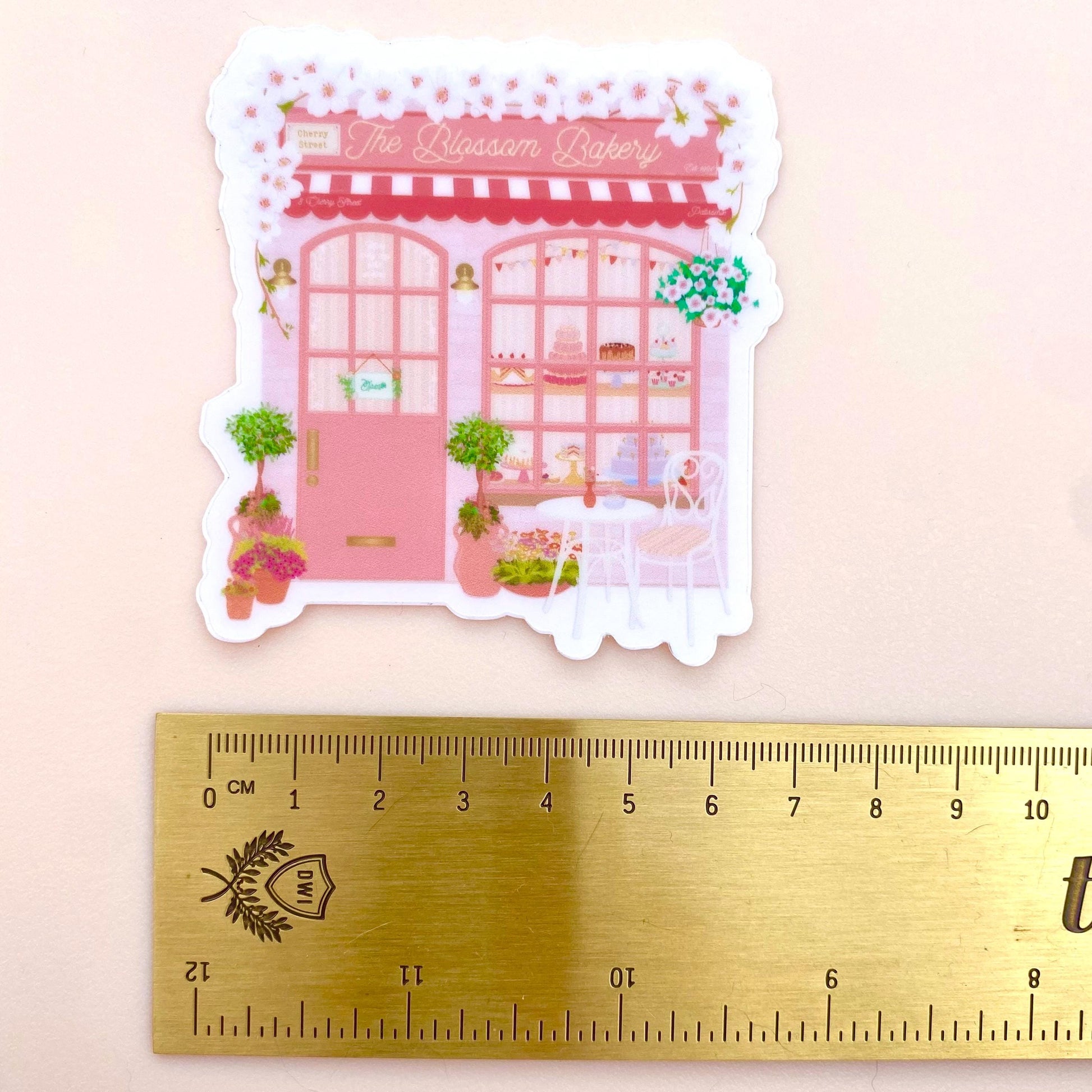 Sticker of a pink bakery with a ruler for scale on a light pink background