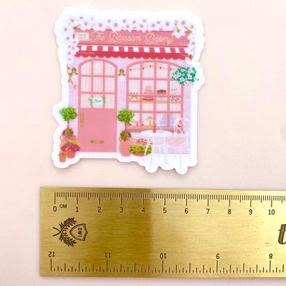 Sticker of a pink bakery with a ruler for scale on a light pink background