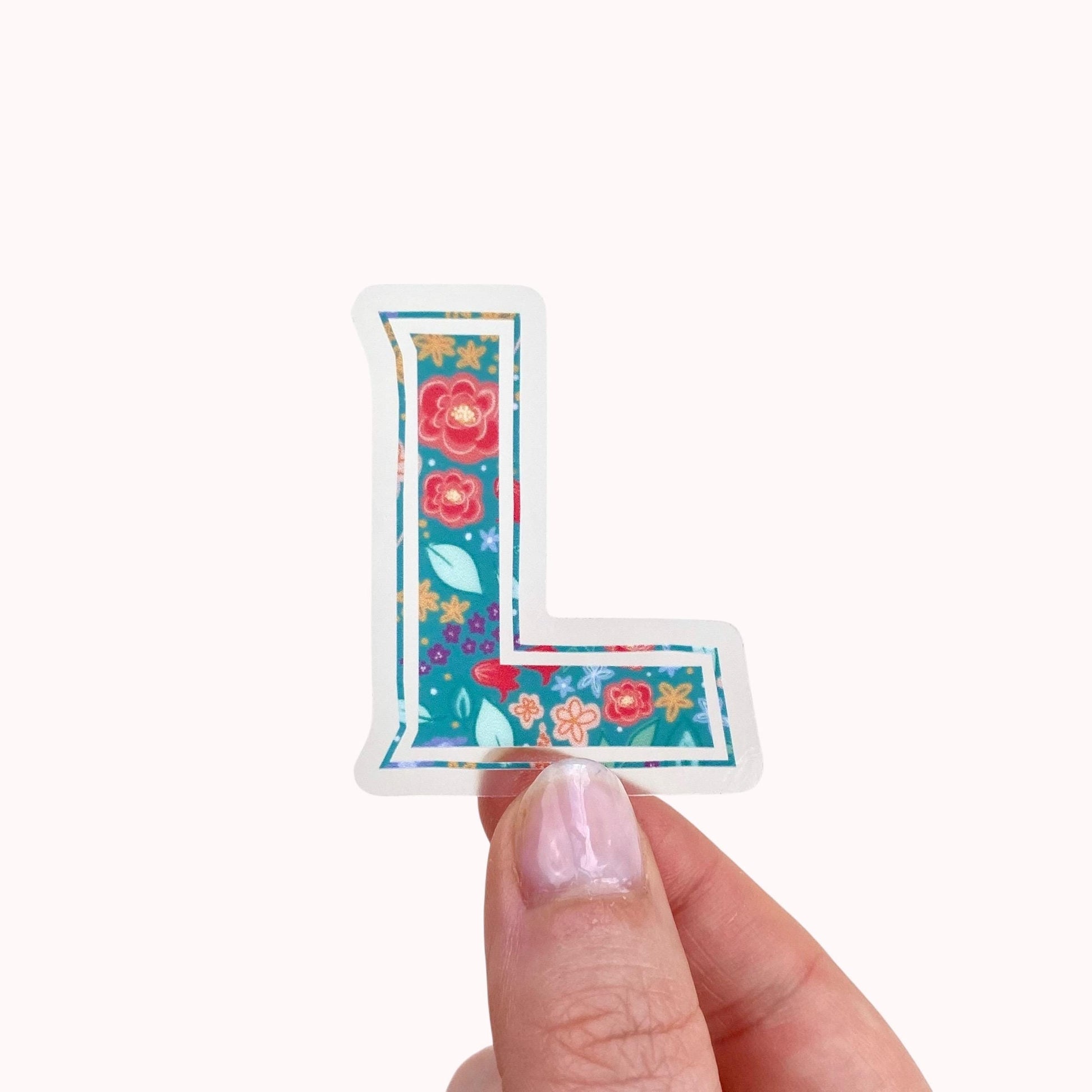 Floral letter 'L' sticker held by a hand on a white background