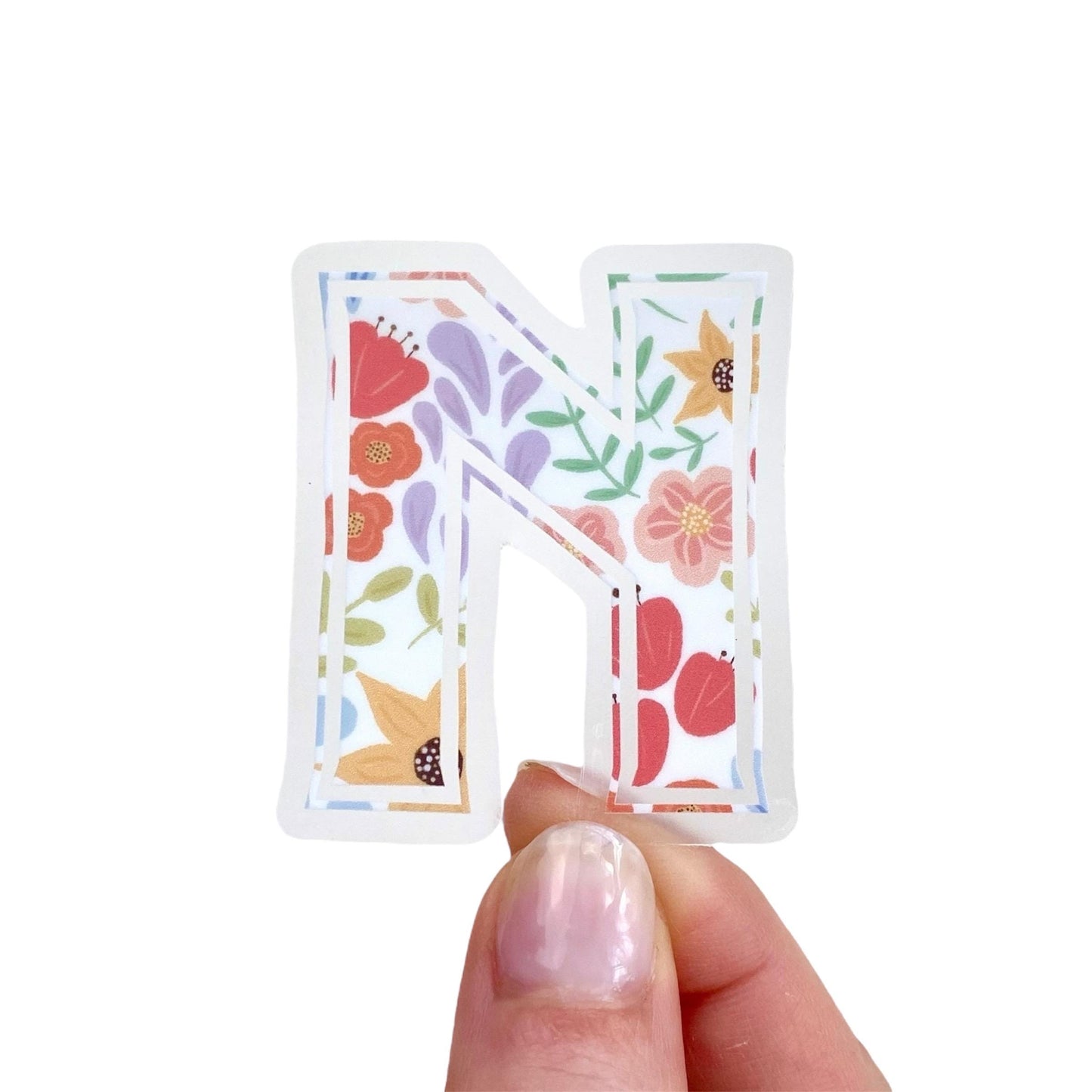 Floral-patterned letter 'N' sticker held by a hand on a white background