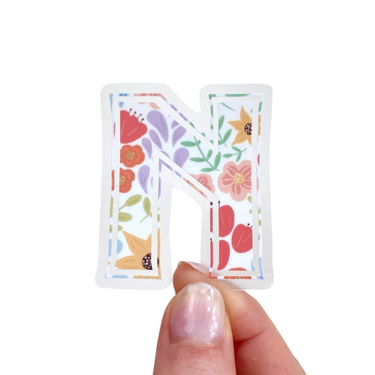 Floral-patterned letter 'N' sticker held by a hand on a white background