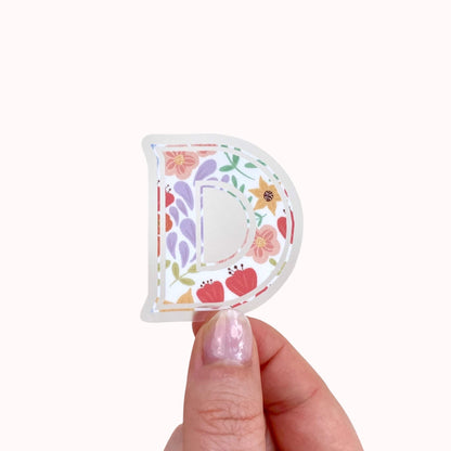 Decorative letter 'P' sticker with floral designs held by a hand on a white background