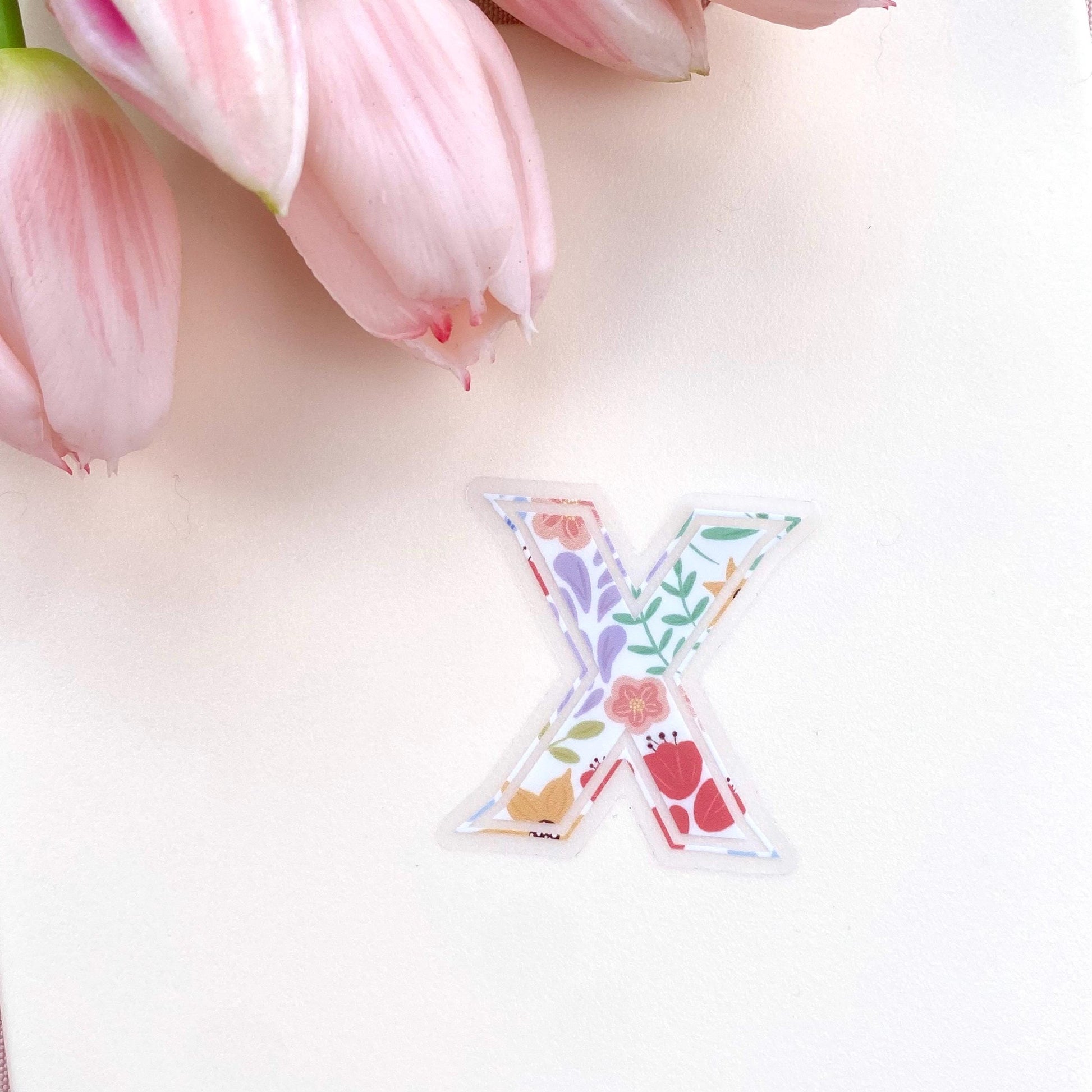 Decorative letter 'X' sticker with floral patterns on a light background with pink tulips.