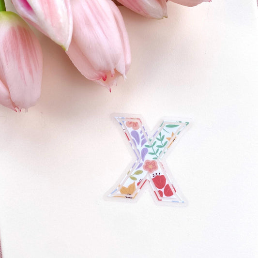 Decorative letter 'X' sticker with floral patterns on a light background with pink tulips.
