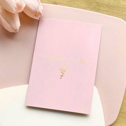Pink greeting card with gold text and floral design on a light pink surface with tulips.