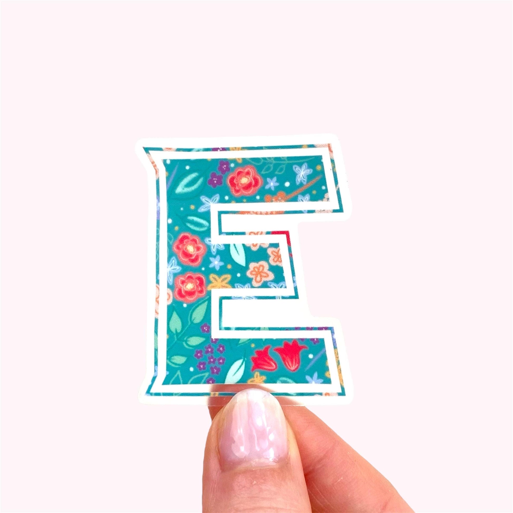 Floral letter 'E' sticker held between thumb and forefinger on a white background