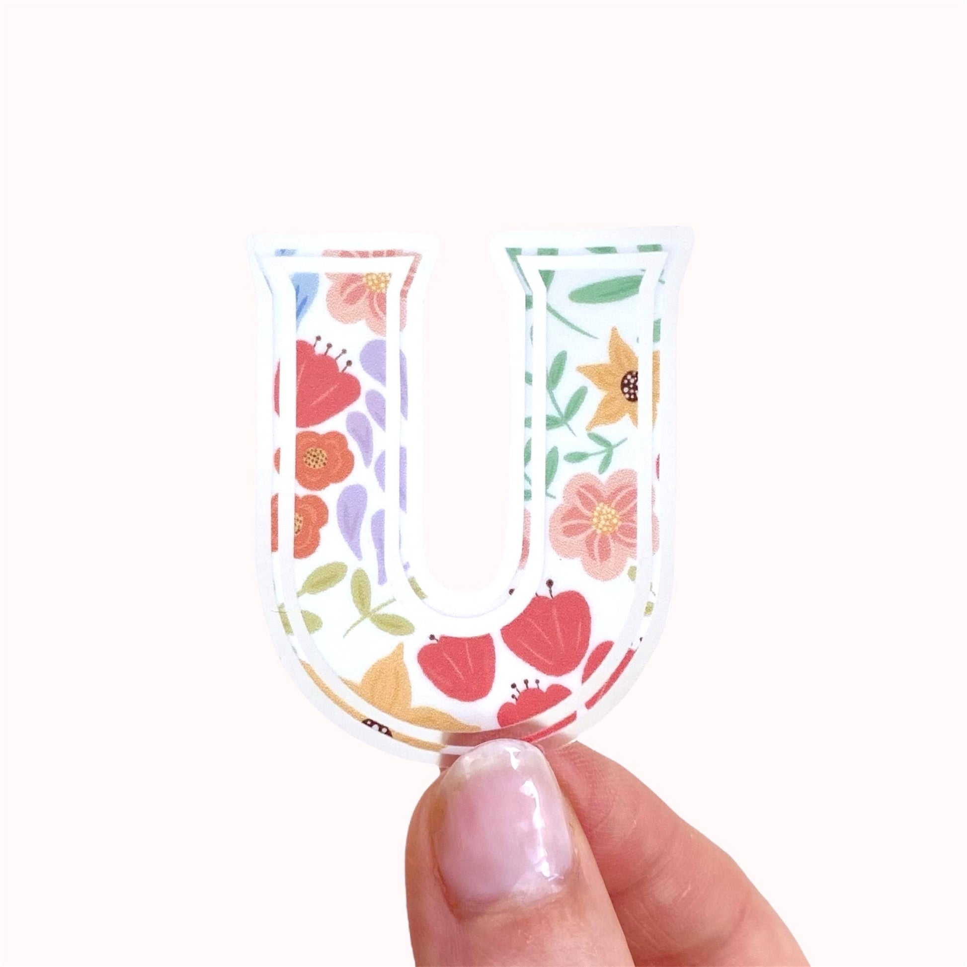 Floral-patterned letter 'U' sticker held by a hand on a white background