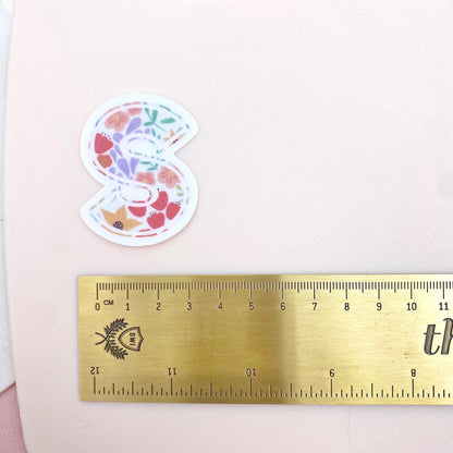 Decorative letter 'S' sticker with floral pattern on a white background with a gold ruler for scale.