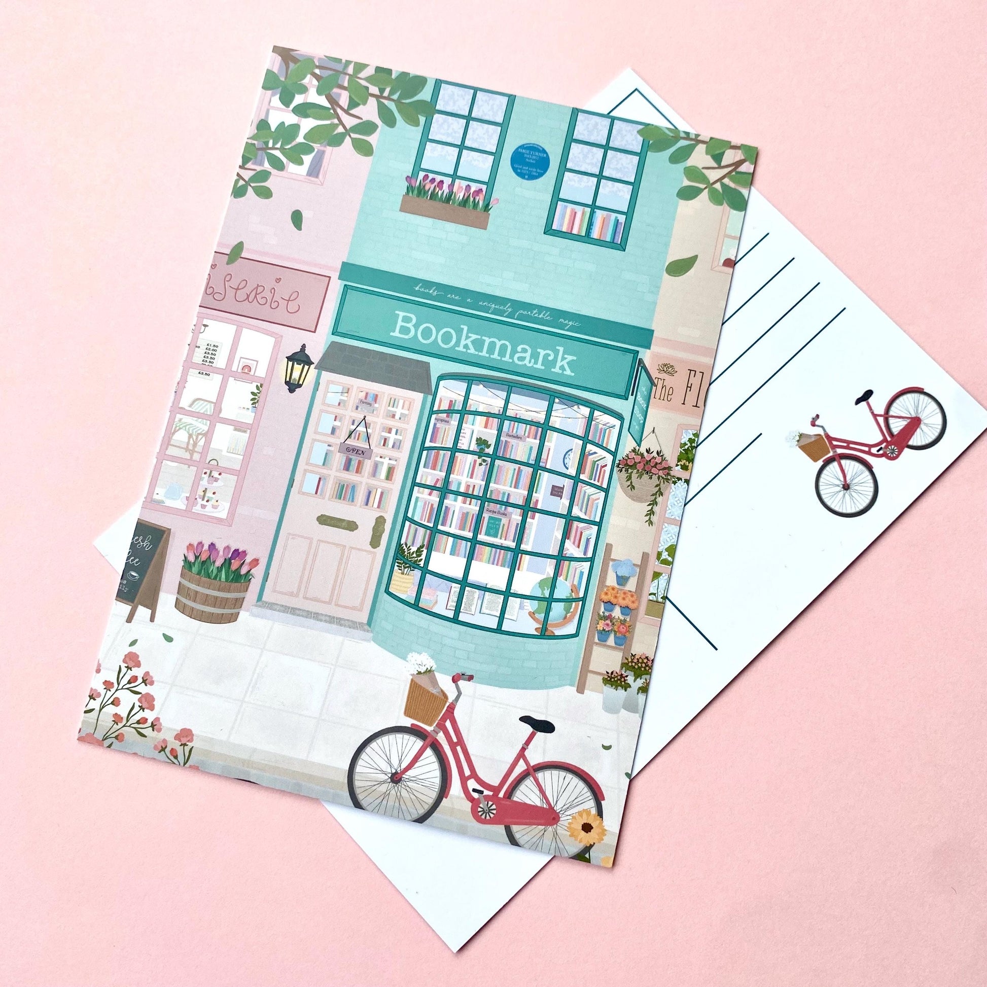 Postcard with a cute illustration of a bookshop and bicycle on a pink background