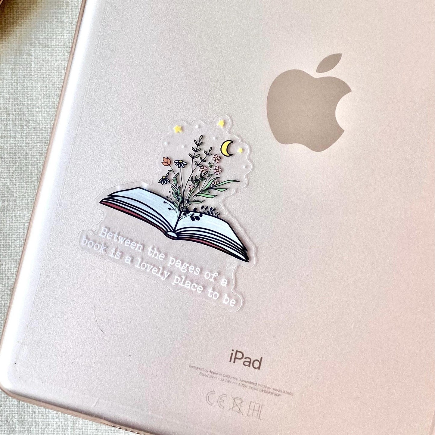 Apple iPad with a decorative sticker featuring a book and flowers on a light background