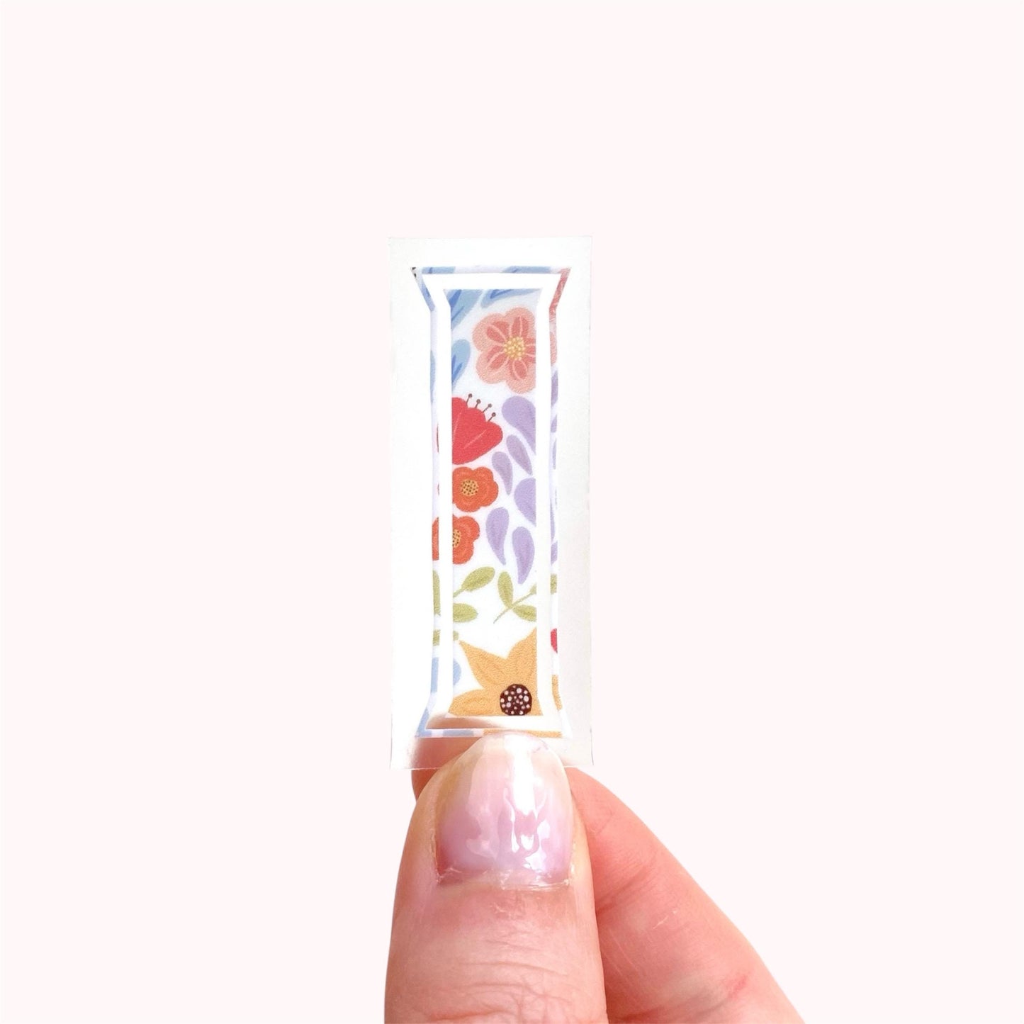 Hand holding a floral-patterned letter 'I' sticker against a white background