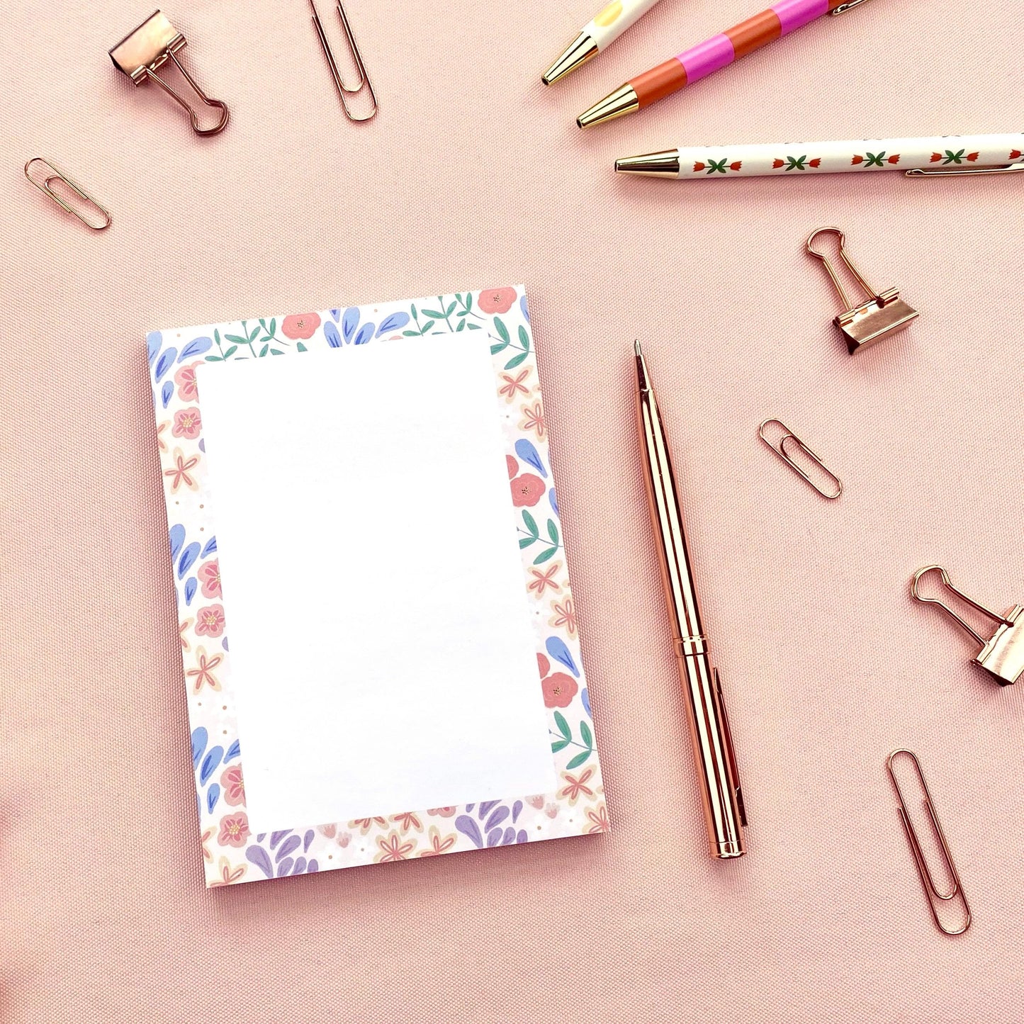 Floral notepad with pens and paper clips on a pink background