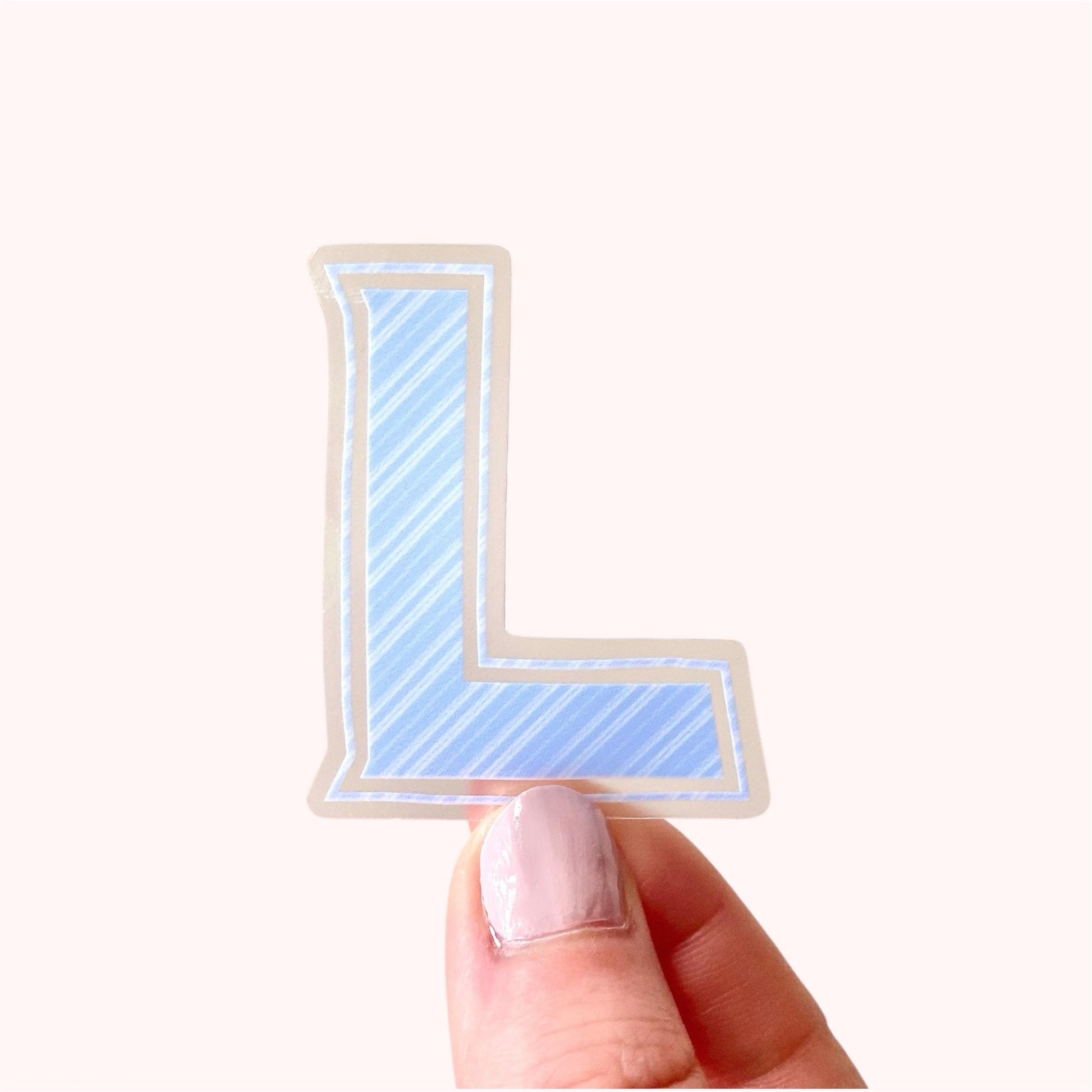 Hand holding a blue striped letter 'L' sticker on a white background
