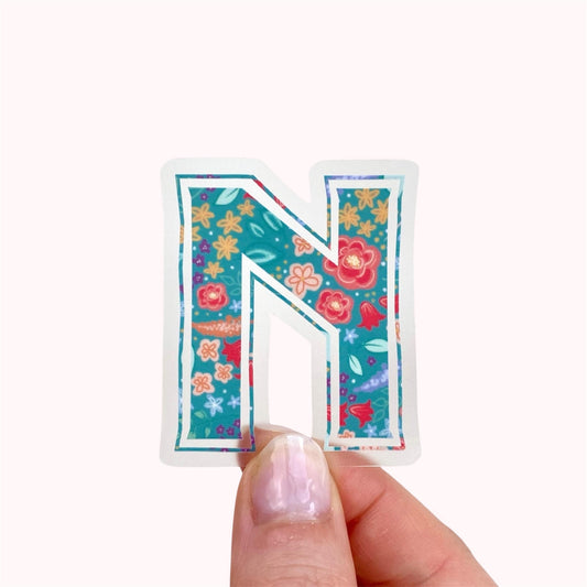 Colourful floral letter 'N' sticker held by a hand on a white background