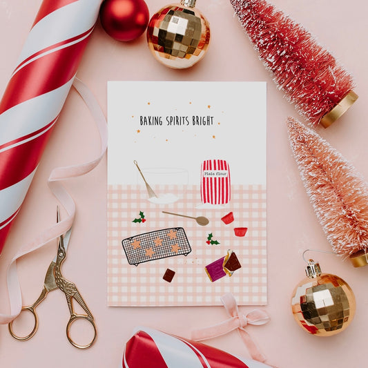 Card with baking-themed illustration surrounded by Christmas decorations on a pink background