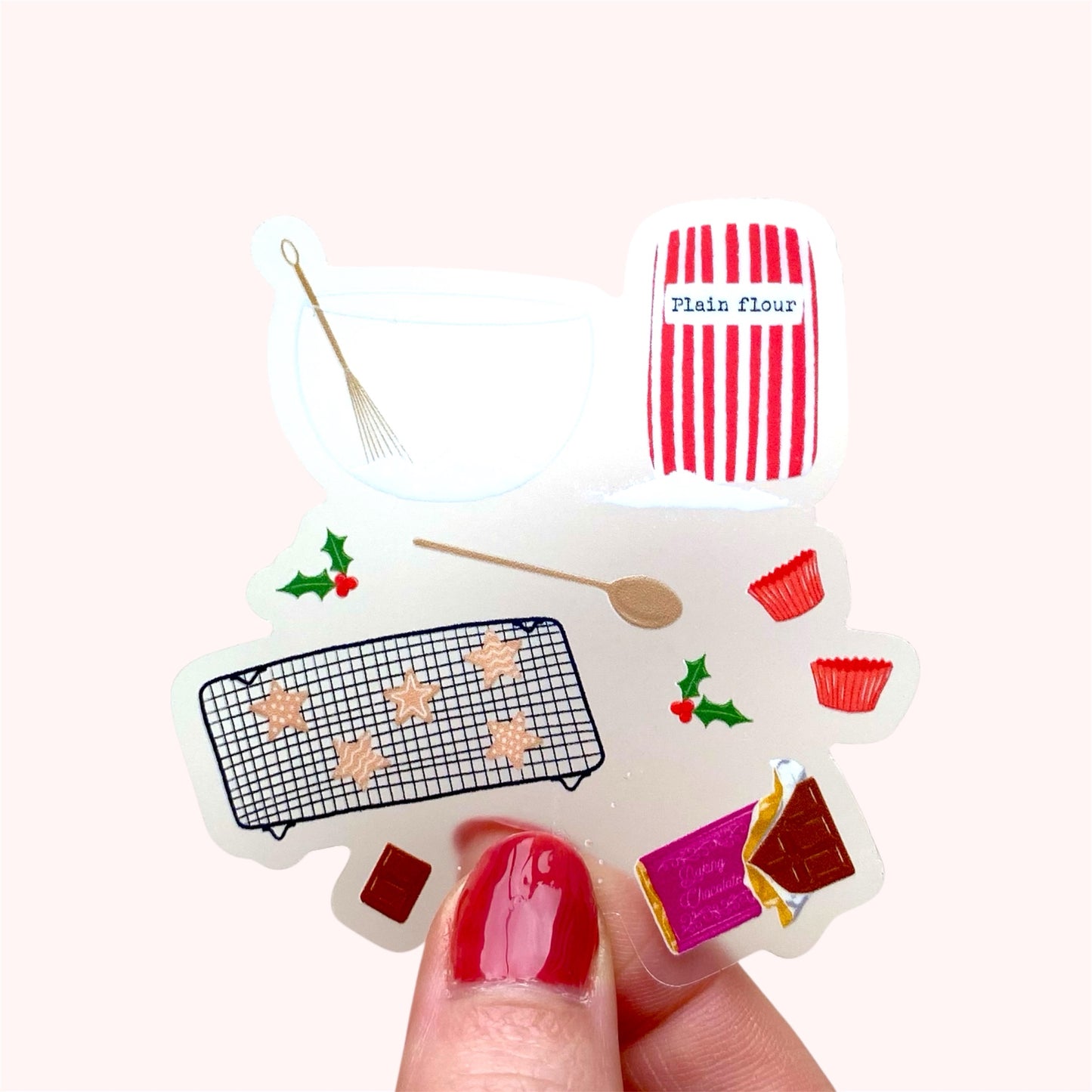 A sticker with an illustration of christmas baking set with a red and white striped flour bag, wooden spoon, mixing bowl and whisk, and star shaped cookies, held up against a pink background.