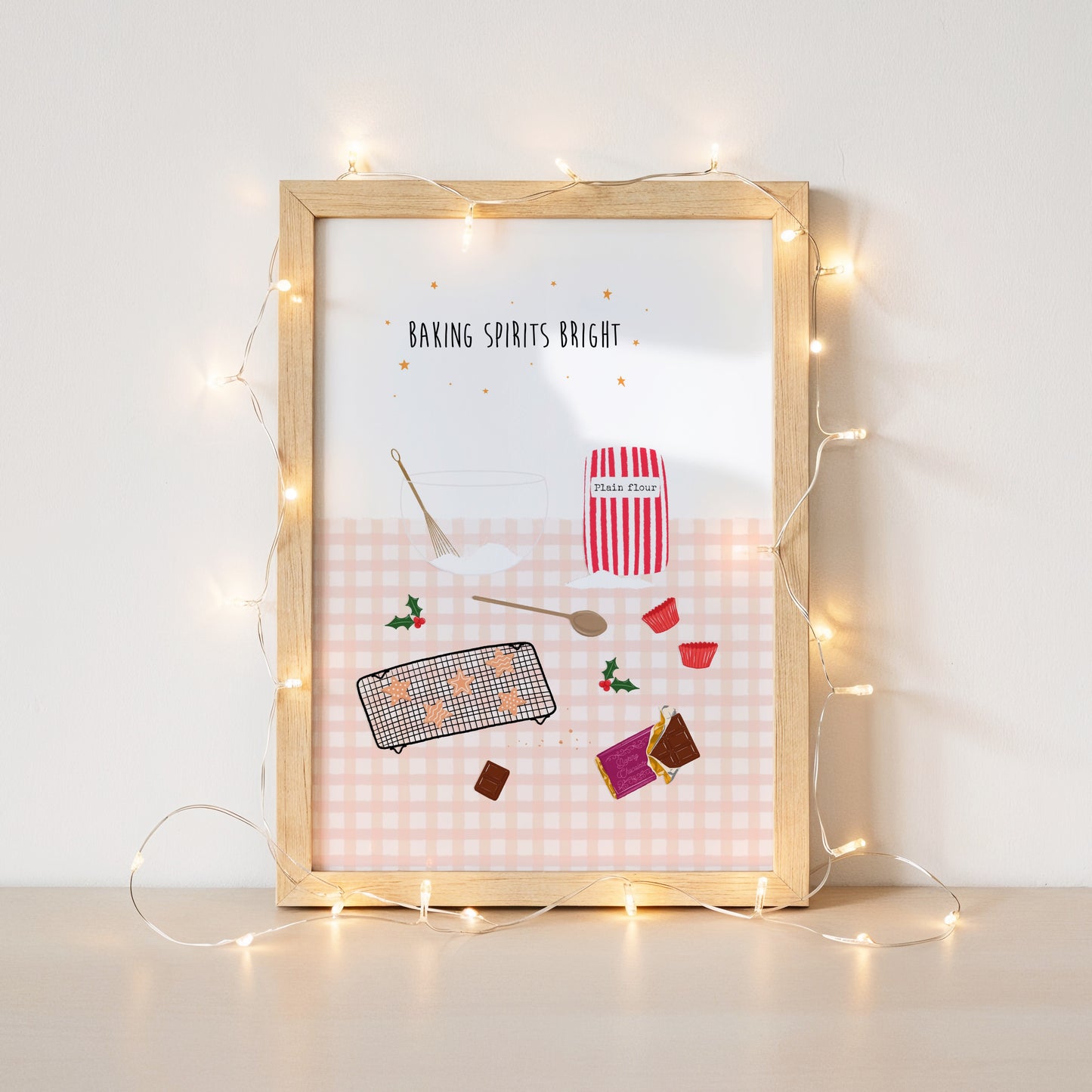Framed artwork with Christmas baking-themed illustrations and string lights on a white wall.