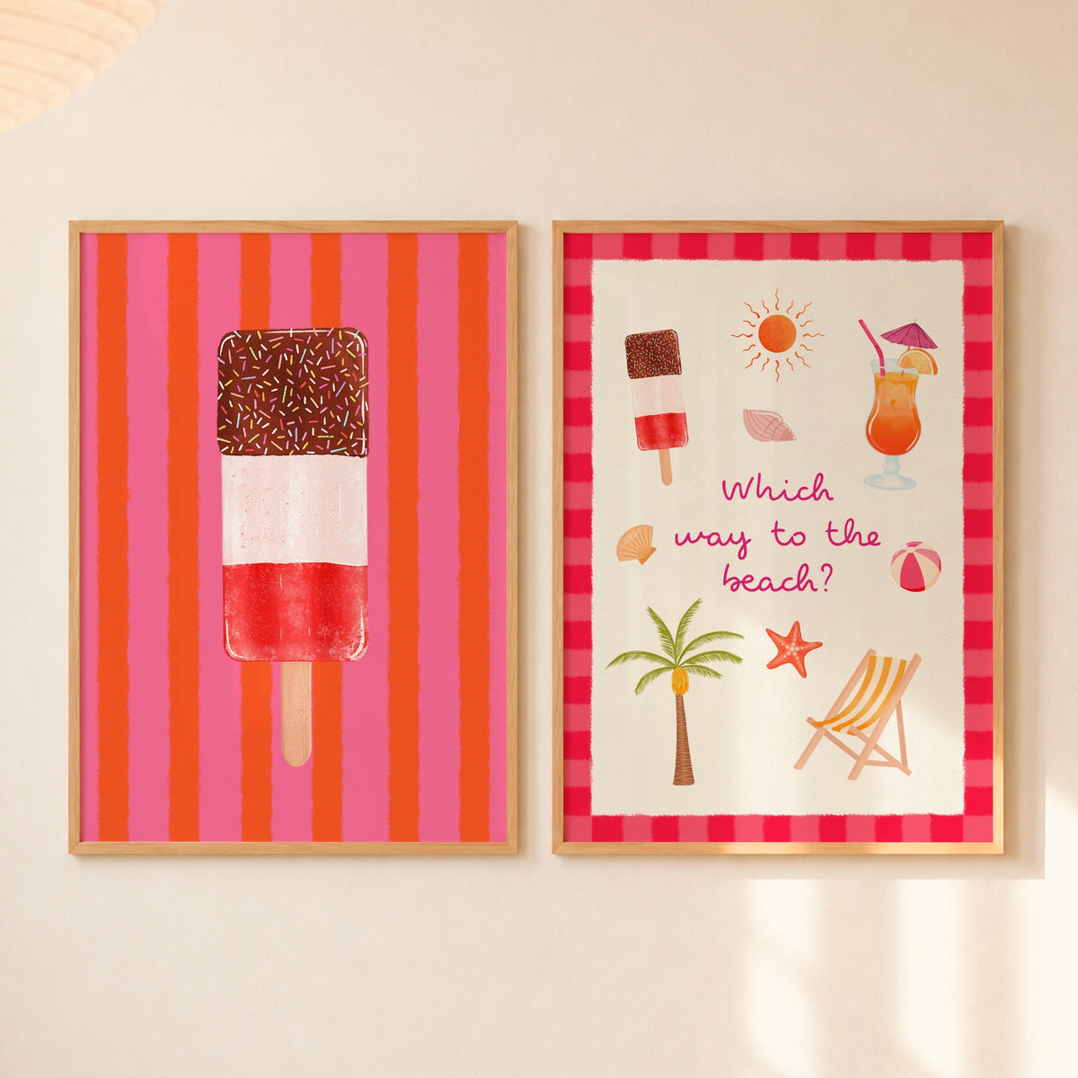 Two framed art prints displayed side-by-side on a warm off-white wall. The left print features an ice lolly with sprinkles on a background of vertical pink and orange stripes. The right print has beach illustrations with text saying ‘Which way to the beach?’ and a pink and red striped border.