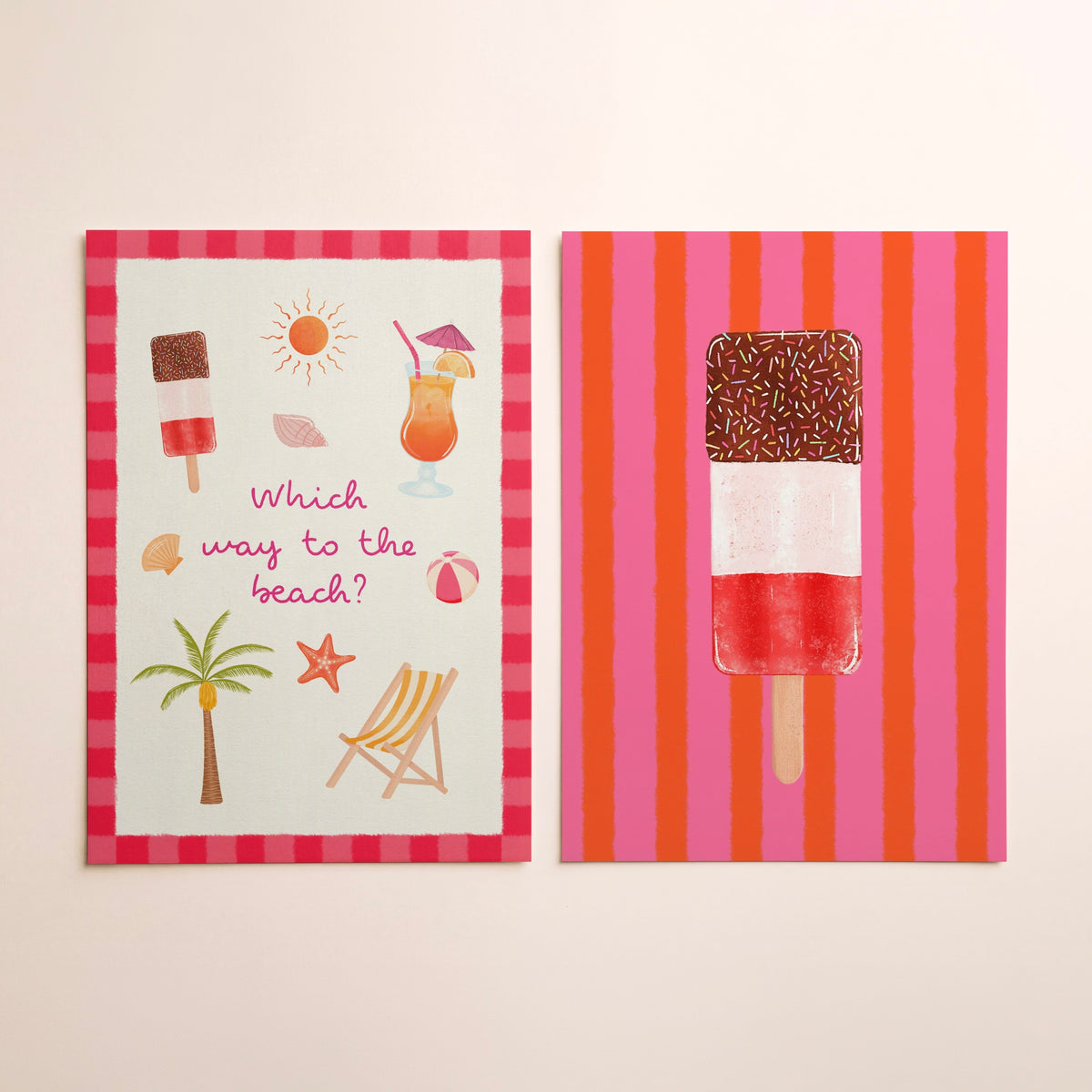 Two square wall art prints with a beach-themed design, displayed side-by-side against a plain off-white wall. The left print features a red and white striped border with illustrations of an ice lolly, cocktail, sun, palm tree, beach chair, and starfish, along with the text 'Which way to the beach?'. The right has an ice lolly with sprinkles against a pink and orange striped background.