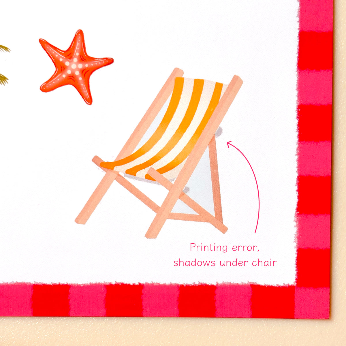 A printed illustration of a beach chair with a starfish on a white background, bordered by a red-and-pink striped pattern. Pink text reads 'Printing error, shadows under chair' with a curved arrow pointing to the chair.