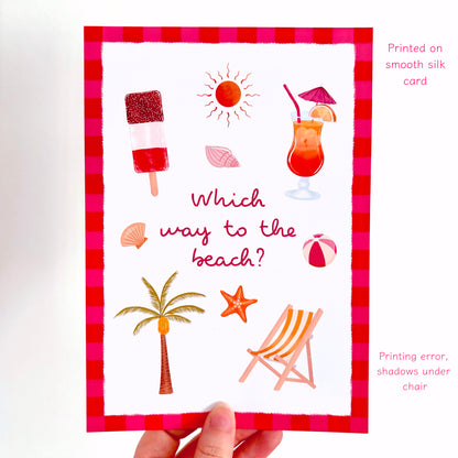 A hand holds a white silk greeting card featuring a red and pink gingham border and summer-themed illustrations including an ice lolly, sun, cocktail, beach umbrellas, palm tree, starfish, and deck chair. Text on the right notes it is printed on a smooth silk card and mentions a printing error and shadow under the chair.