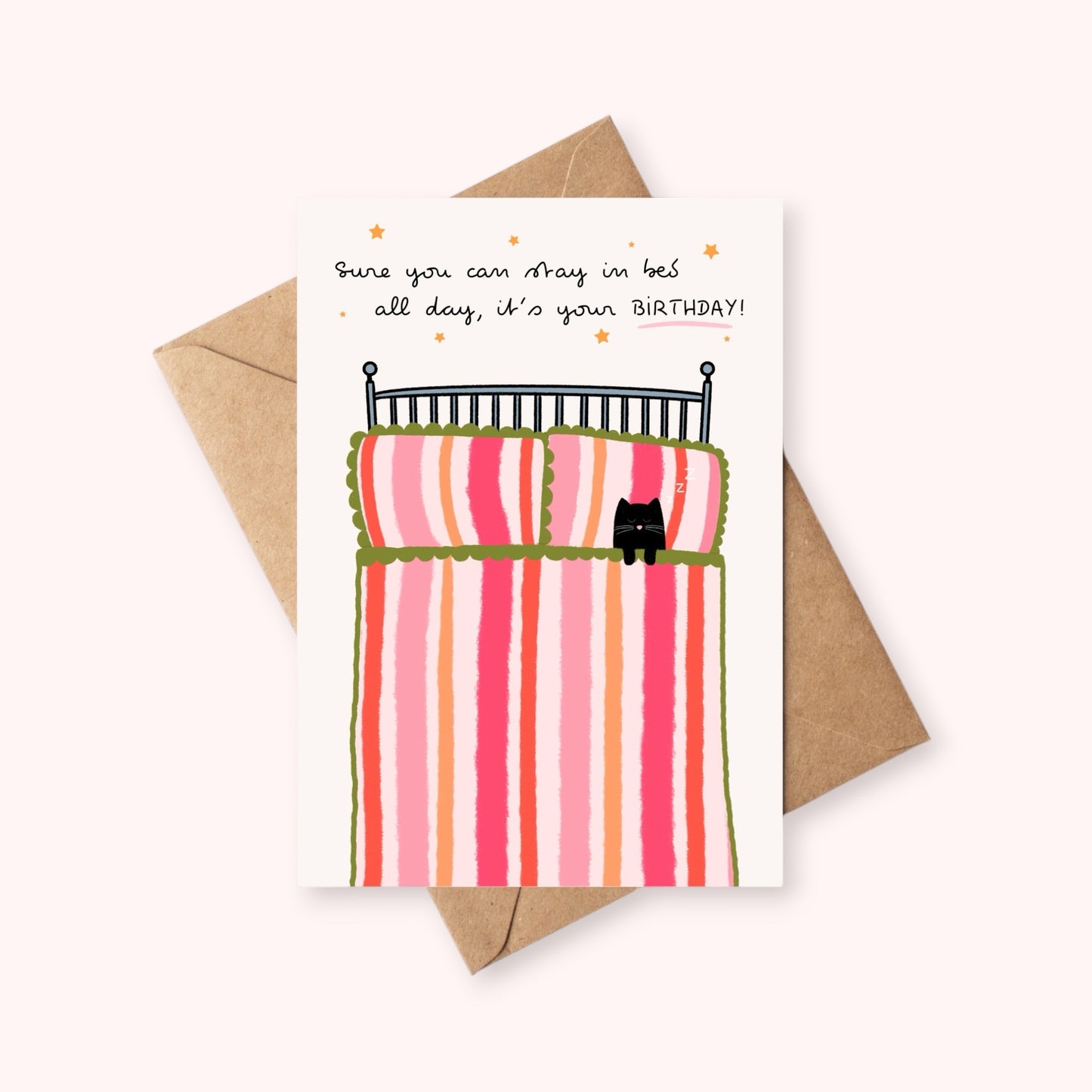 Birthday card with a bed and cat illustration with a 'Sure you can stay in bed all day, it's your birthday!' quote, and a brown envelope on a pink background