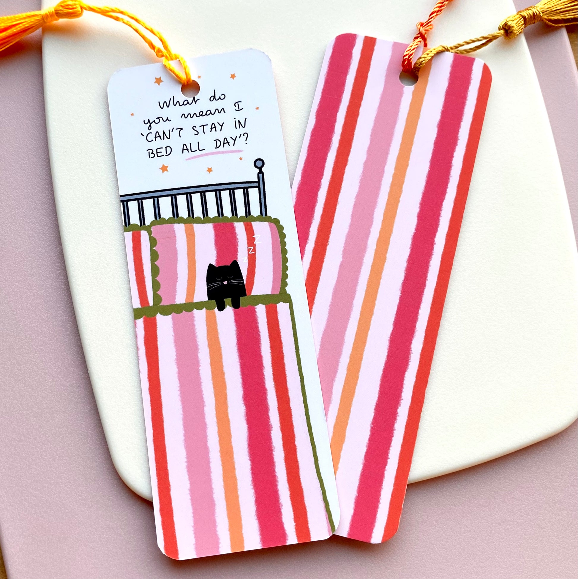 Pink and orange striped bookmark with cartoon cat and 'What do you mean I 'can't stay in bed all day'' text with stars on a white background