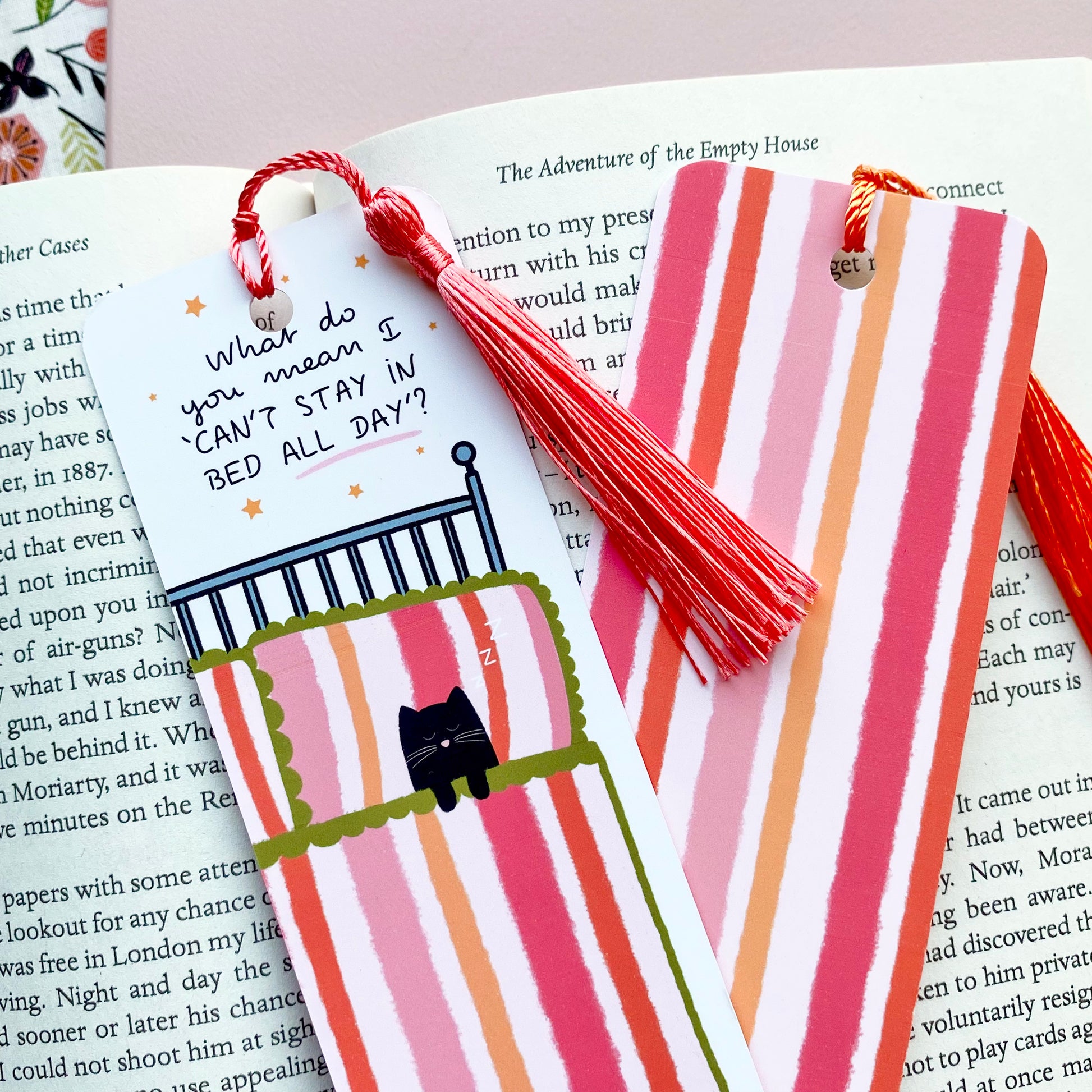 Bookmarks with pink striped cat in bed illustrations and colourful tassels on an open book