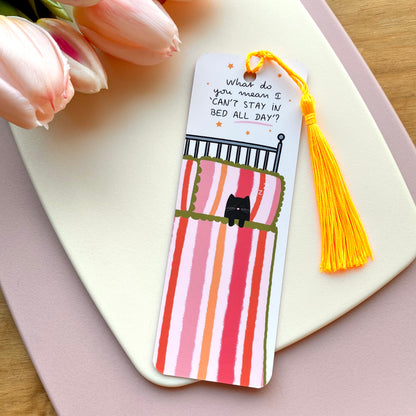 Bookmark with cute cat in bed illustration and bright yellow tassel on a pink surface with tulips