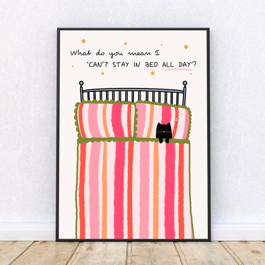 Framed artwork of a bed with striped bedding and a cat, on a white wall, with a quote 'What do you mean I 'can't stay in bed all day'' surrounded by stars.