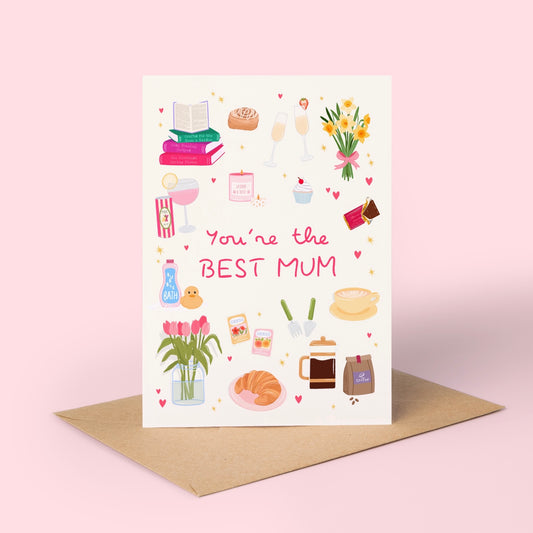 A vertical greeting card with a cream background and colourful illustrated icons around the words 'You're the BEST MUM' in pink script, shown standing upright on a brown kraft envelope against a soft pink backdrop.