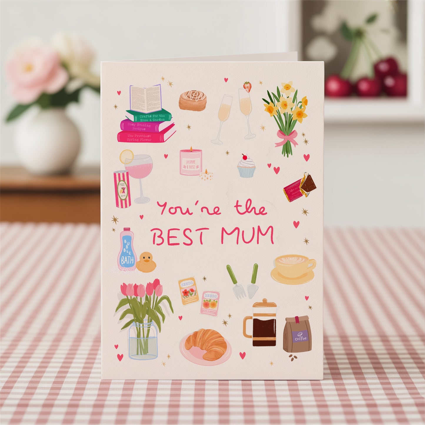 Greeting card with illustrations and text 'You're the BEST MUM' on a pink gingha tablecloth.