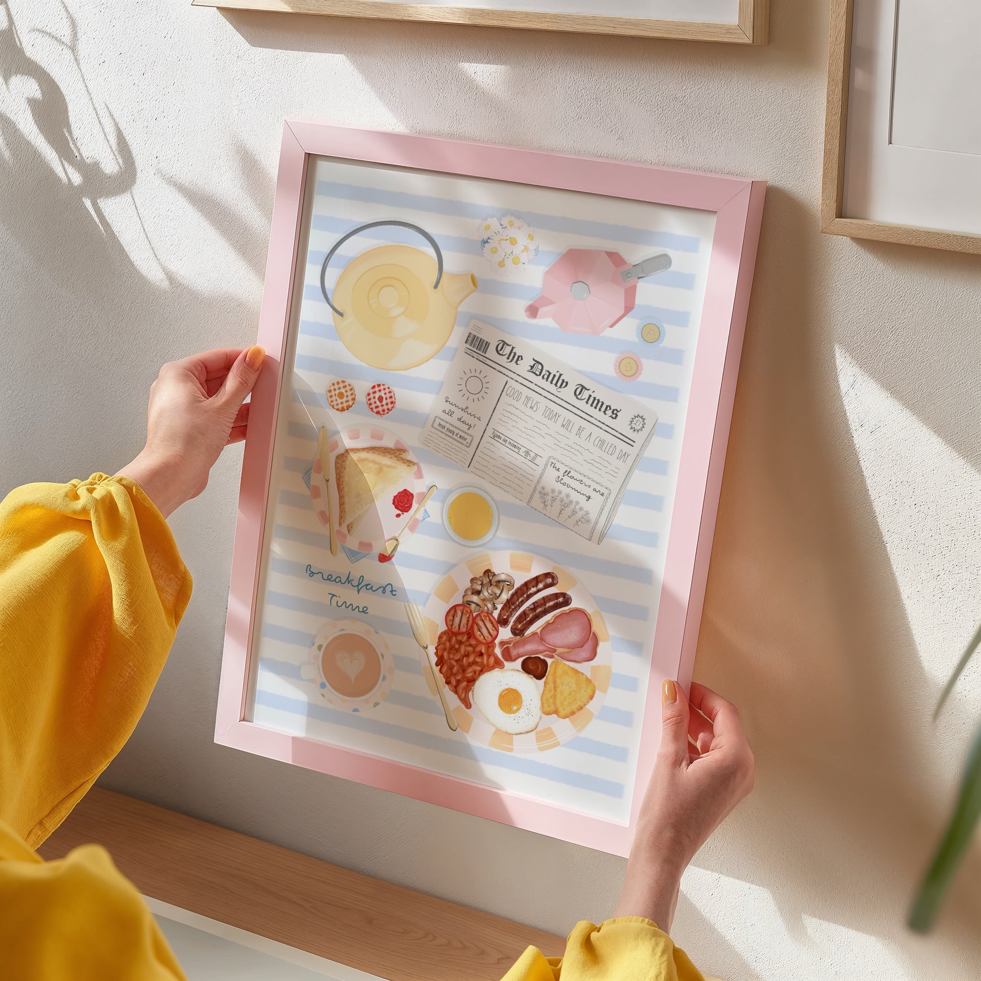 Person holding a framed illustration of breakfast items on a light-colored wall.