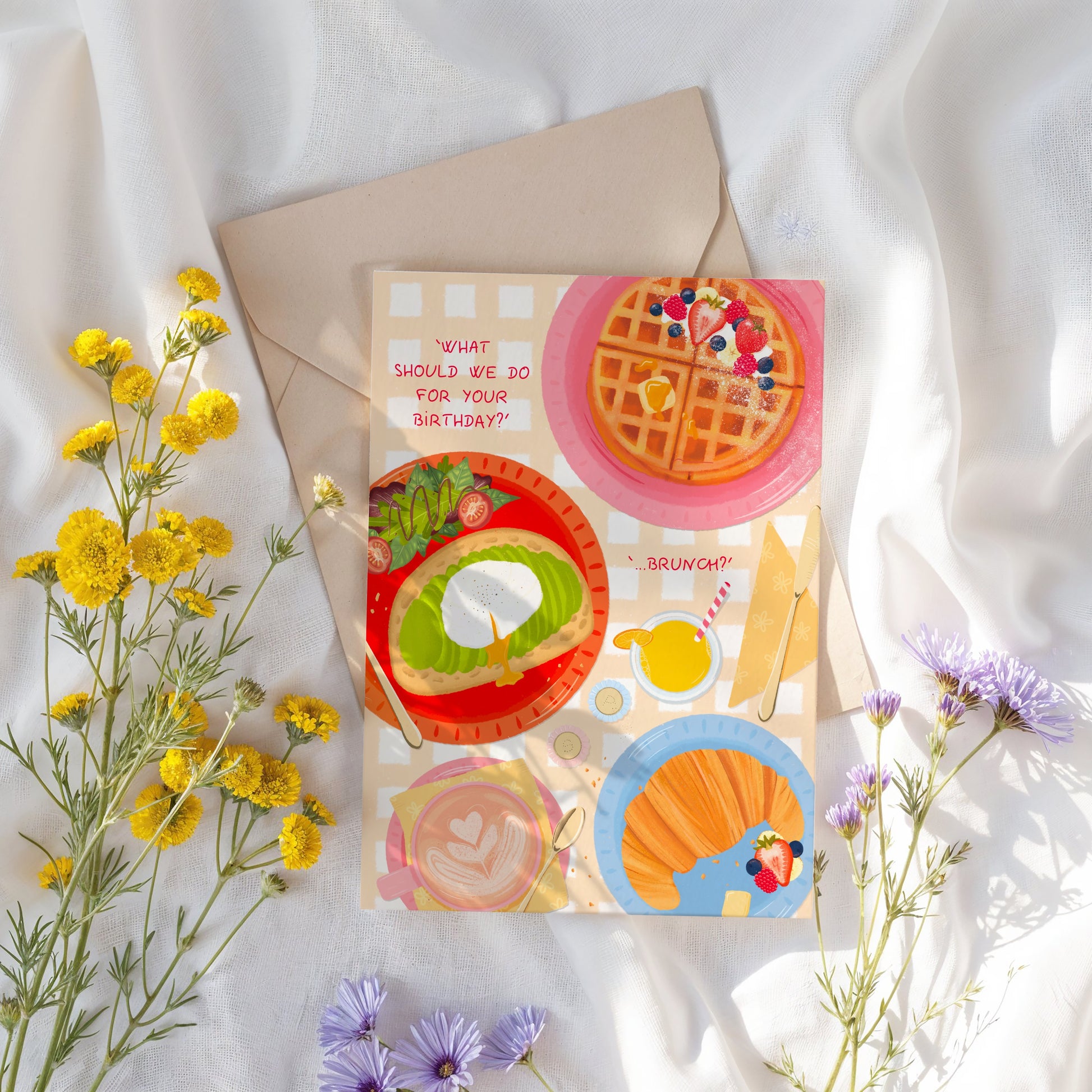 Greeting card with brunch-themed illustrations on a white fabric background with flowers.