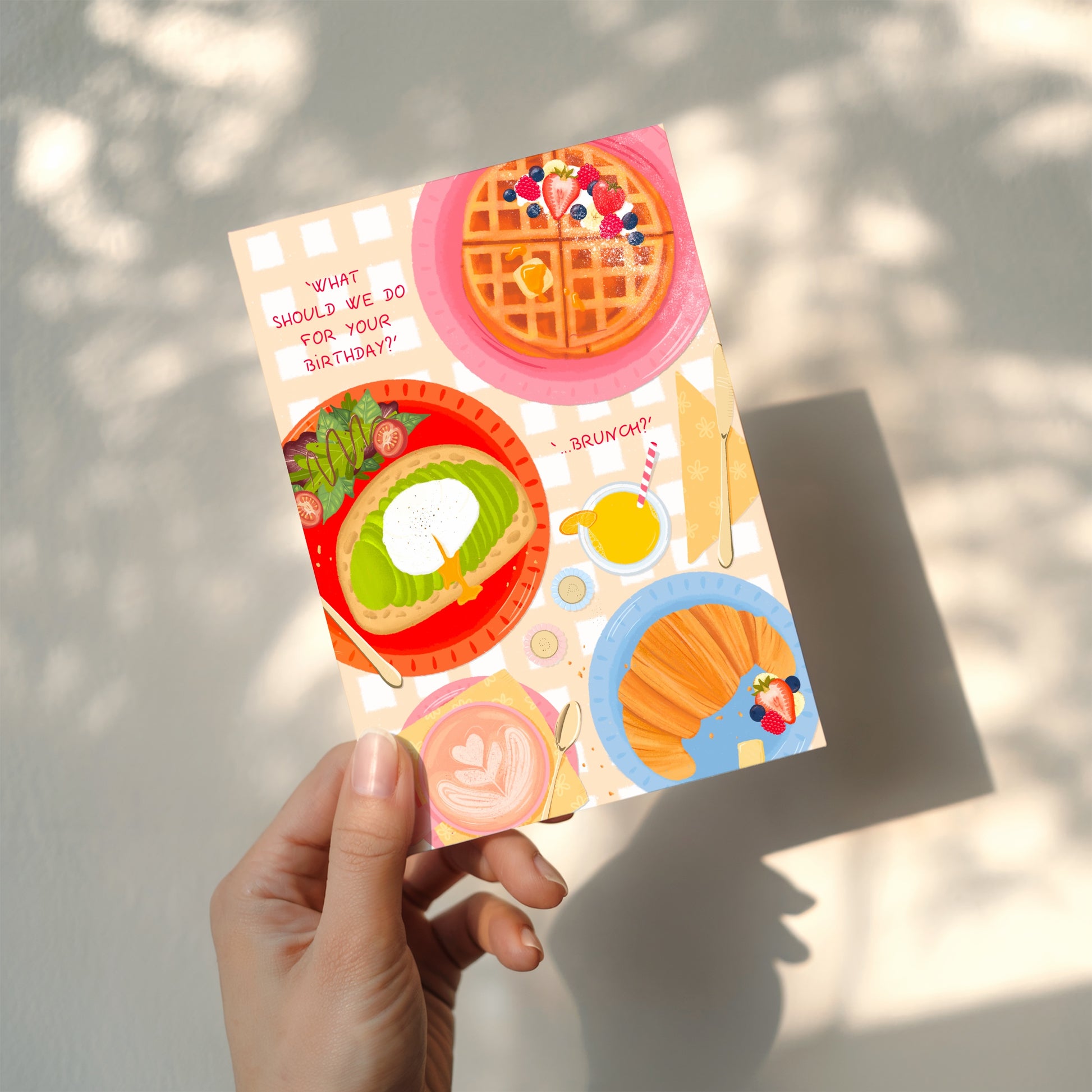 Colourful card with illustrations of brunch food items held by a hand against a light background