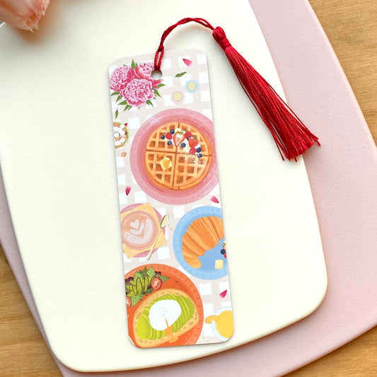Bookmark with avocado toast, latte, croissant and waffle design with a red tassel on a white surface