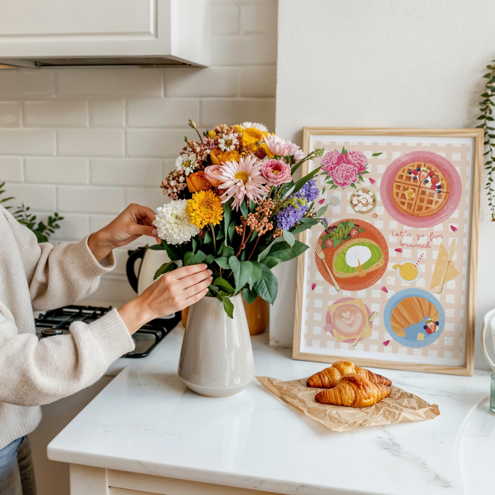 Person arranging flowers in a kitchen with a colourful illustrated brunch print on the wall.