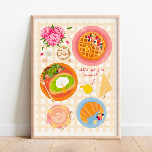 A framed art print featuring a whimsical breakfast illustration with waffles, avocado toast, a croissant with berries, and pink flowers, leaning against a white wall on a light wood floor.