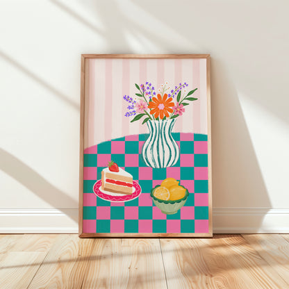 A framed art print featuring a colourful table scene with a striped pink background, a vase of flowers, a slice of cake on a plate, and a bowl of lemons, leaning against a white wall on a light wood floor.
