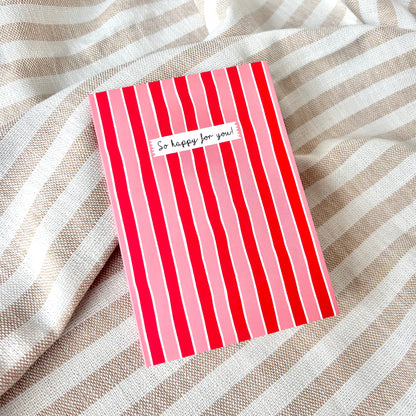 Red and pink striped card with 'So happy for you!' text against a striped fabric background.