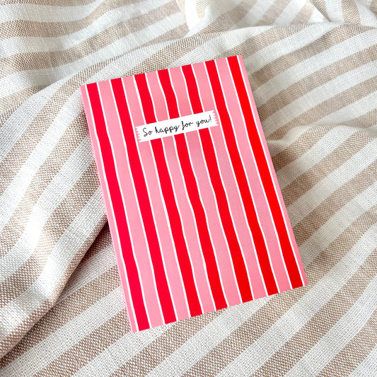 Red and pink striped card with 'So happy for you!' text against a striped fabric background.