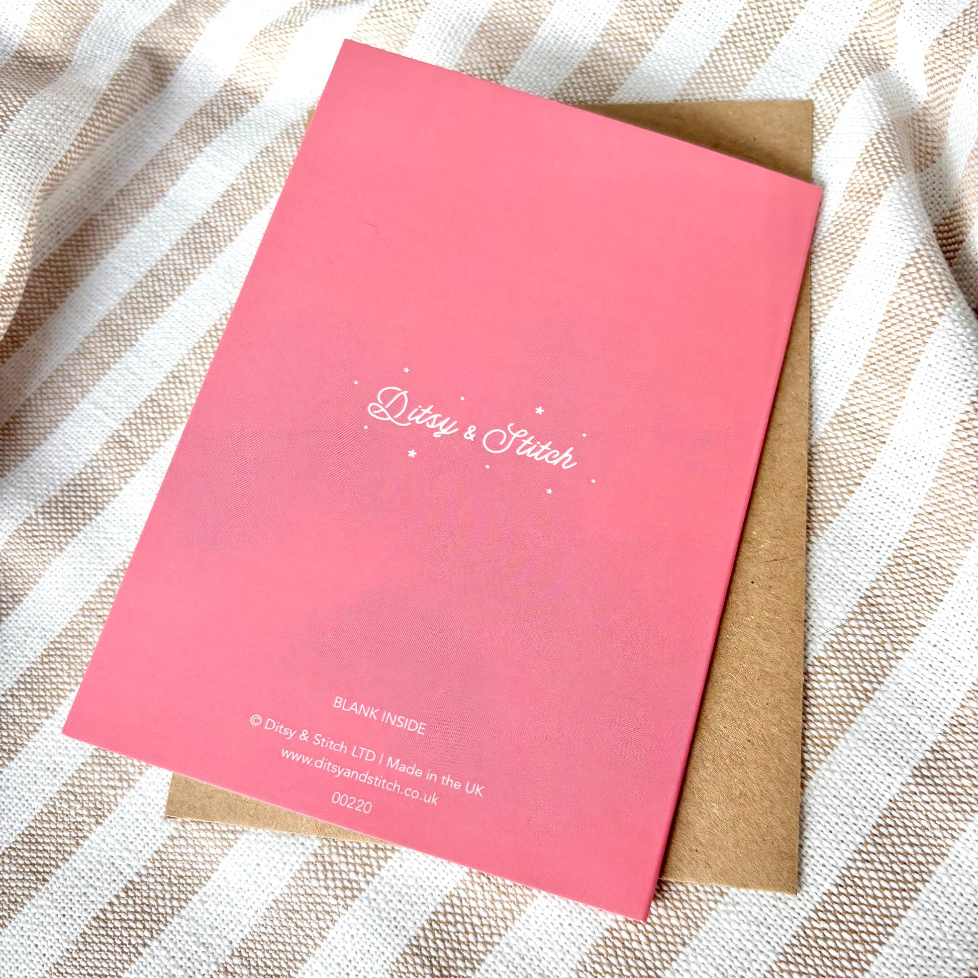 Pink card with 'Ditsy & Stitch' branding on the back, on a striped fabric background