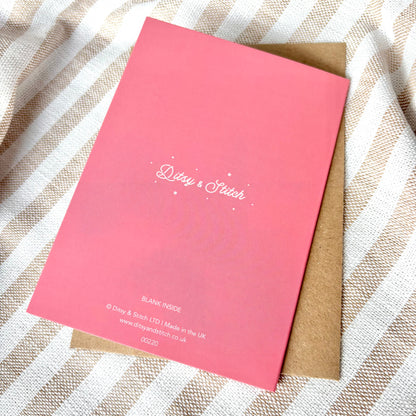 Pink card with 'Ditsy & Stitch' branding on the back, on a striped fabric background